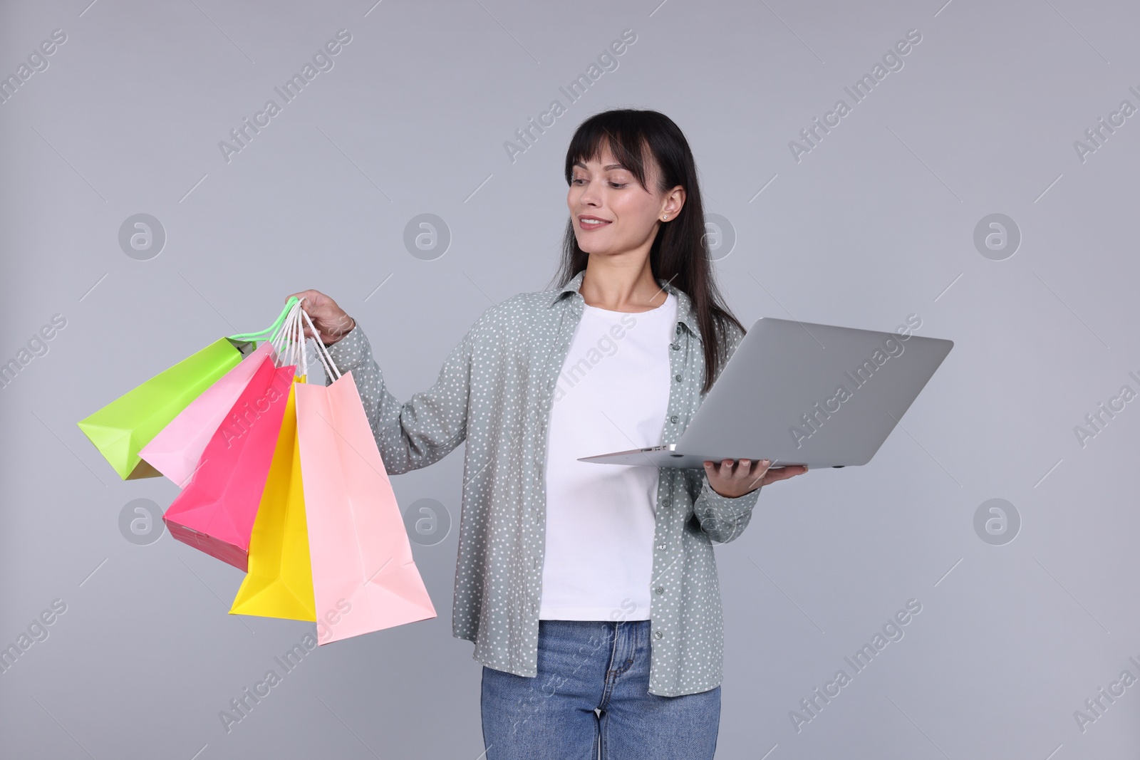 Photo of Internet shopping. Happy woman with laptop and colorful bags on grey background