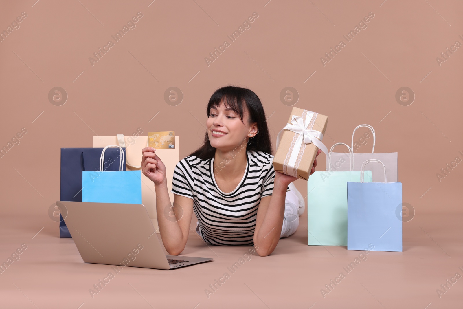 Photo of Internet shopping. Happy woman with credit card, gift box, laptop and colorful bags on beige background