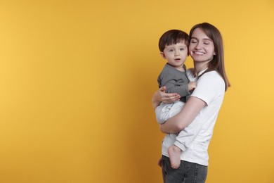 Photo of Happy mother with her cute little son on yellow background, space for text