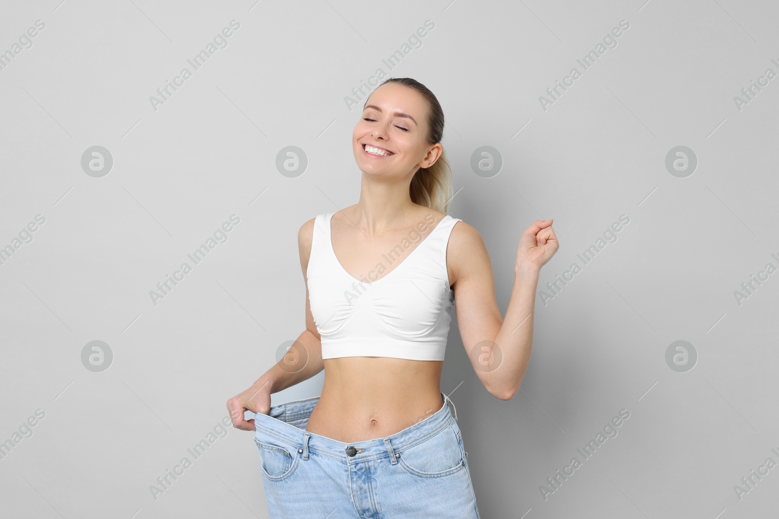 Photo of Weight loss. Happy woman wearing big jeans on light grey background