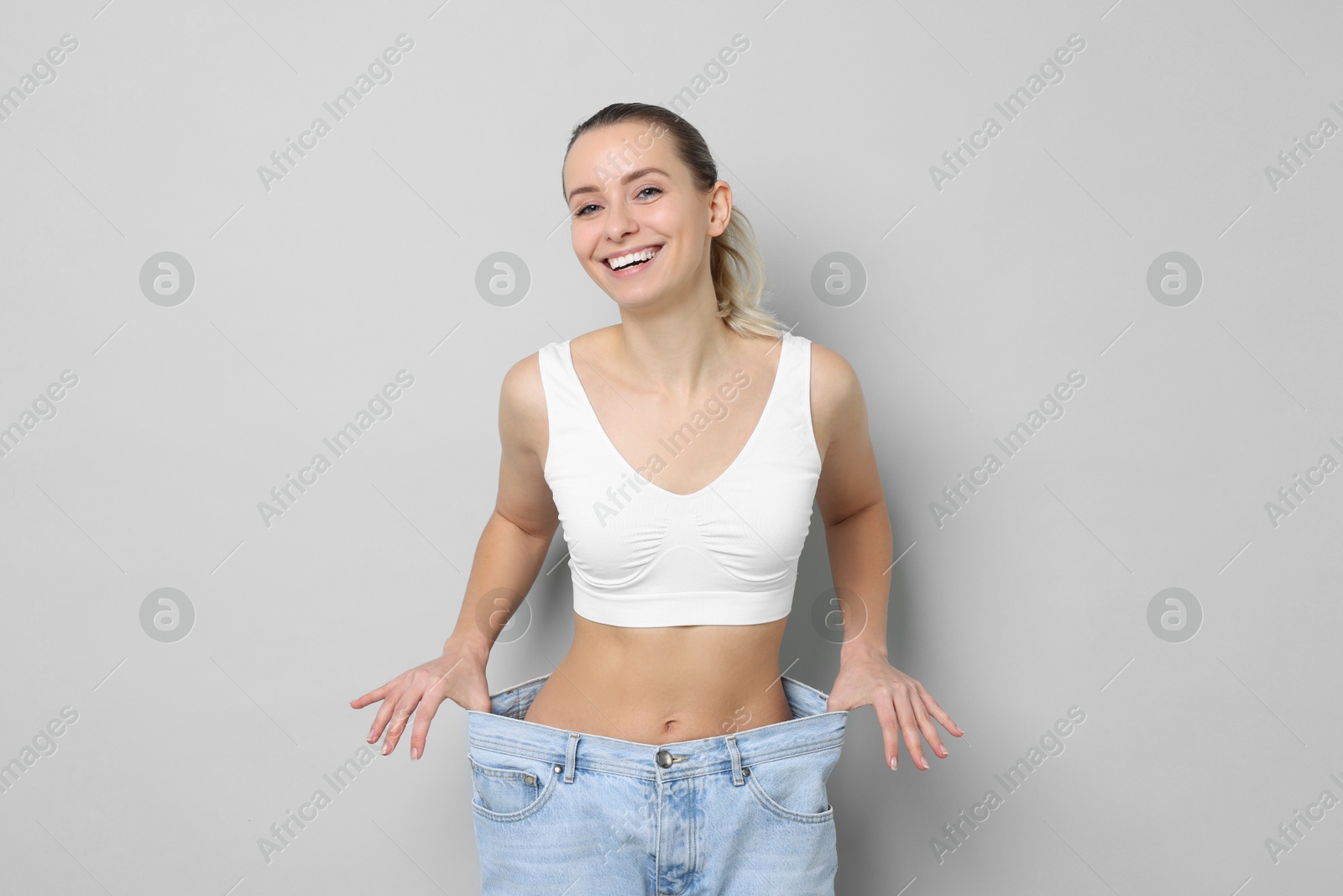 Photo of Weight loss. Happy woman wearing big jeans on light grey background