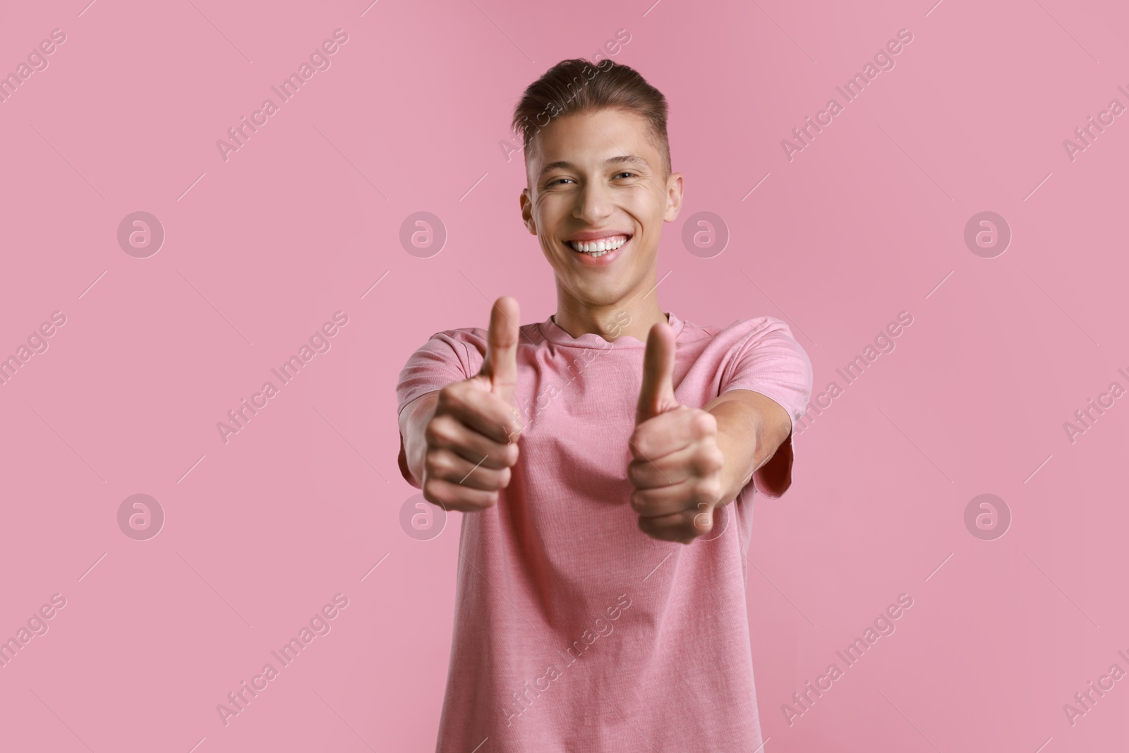 Photo of Happy man showing thumbs up on pink background. Like gesture