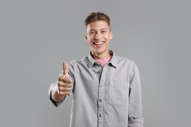 Photo of Happy man showing thumbs up on grey background. Like gesture