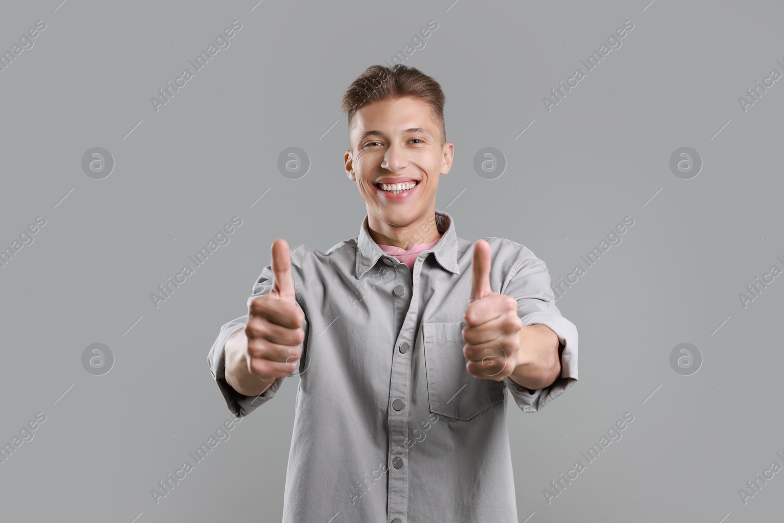 Photo of Happy man showing thumbs up on grey background. Like gesture