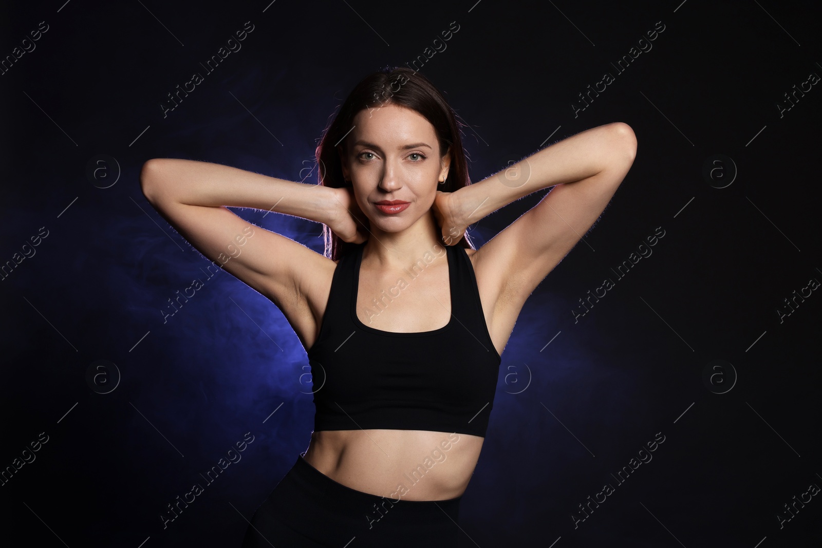 Photo of Beautiful woman in stylish sportswear on dark background with color light and smoke