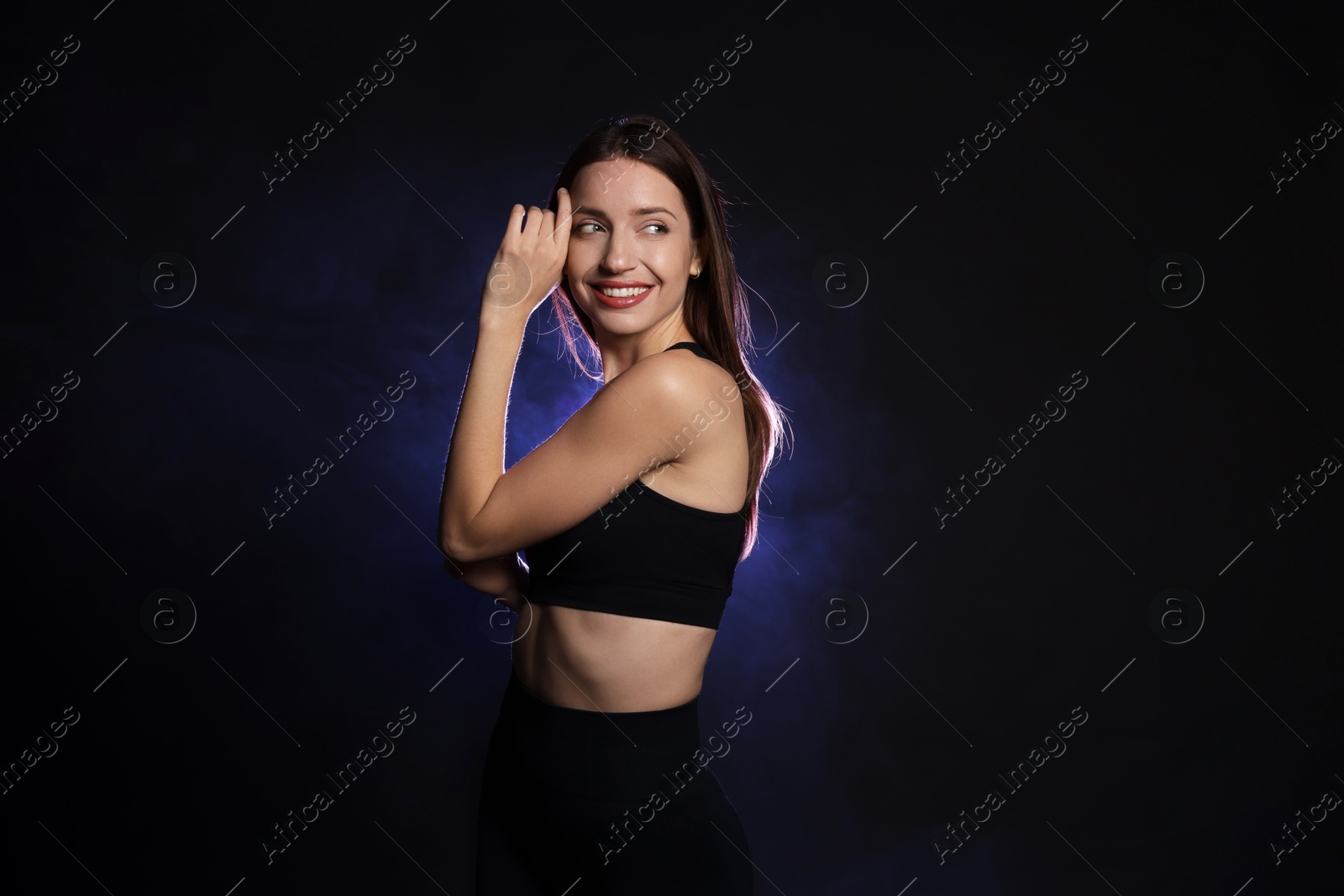 Photo of Beautiful woman in stylish sportswear on dark background with color light and smoke