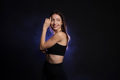 Photo of Beautiful woman in stylish sportswear on dark background with color light and smoke