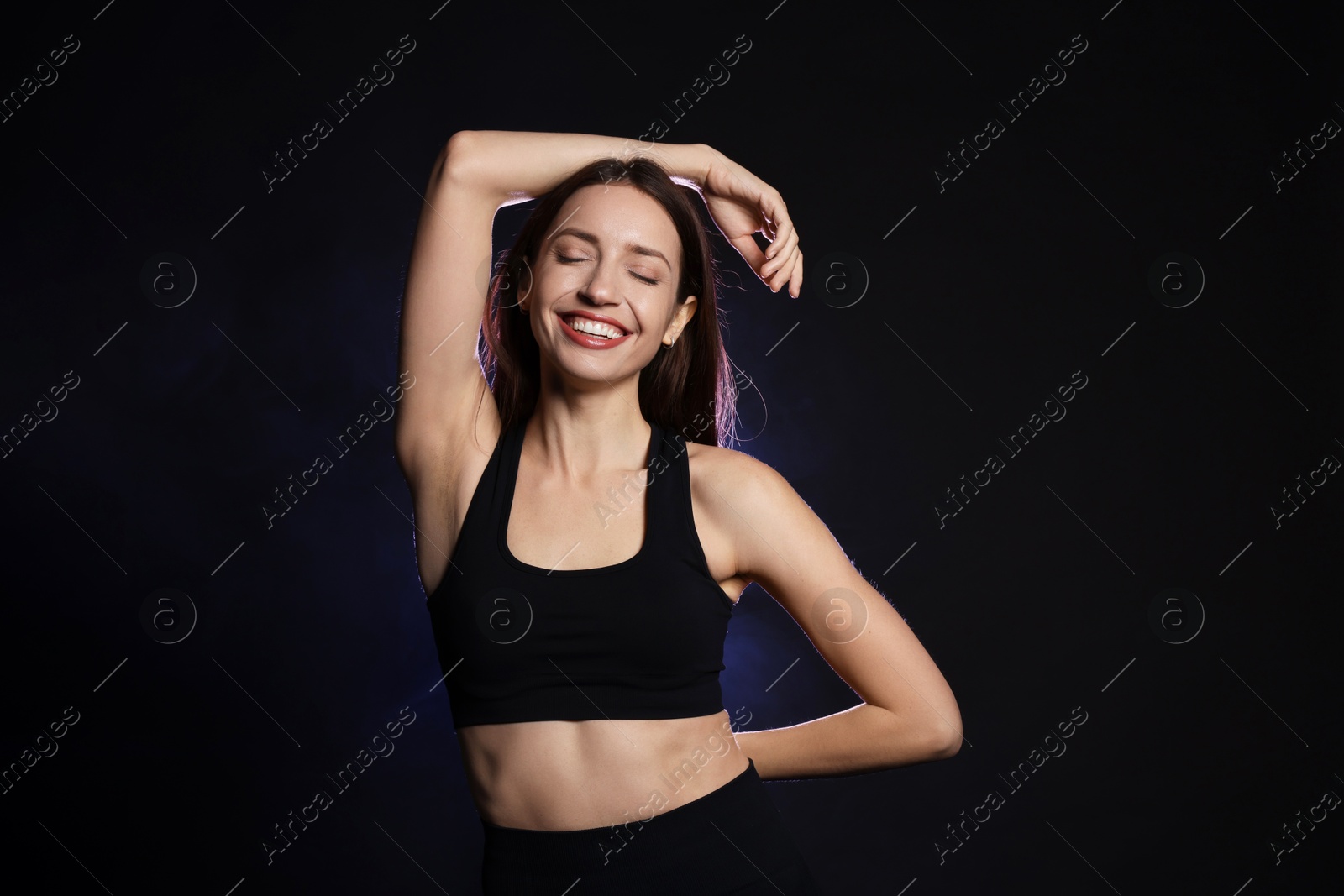 Photo of Beautiful woman in stylish sportswear on dark background with color light and smoke