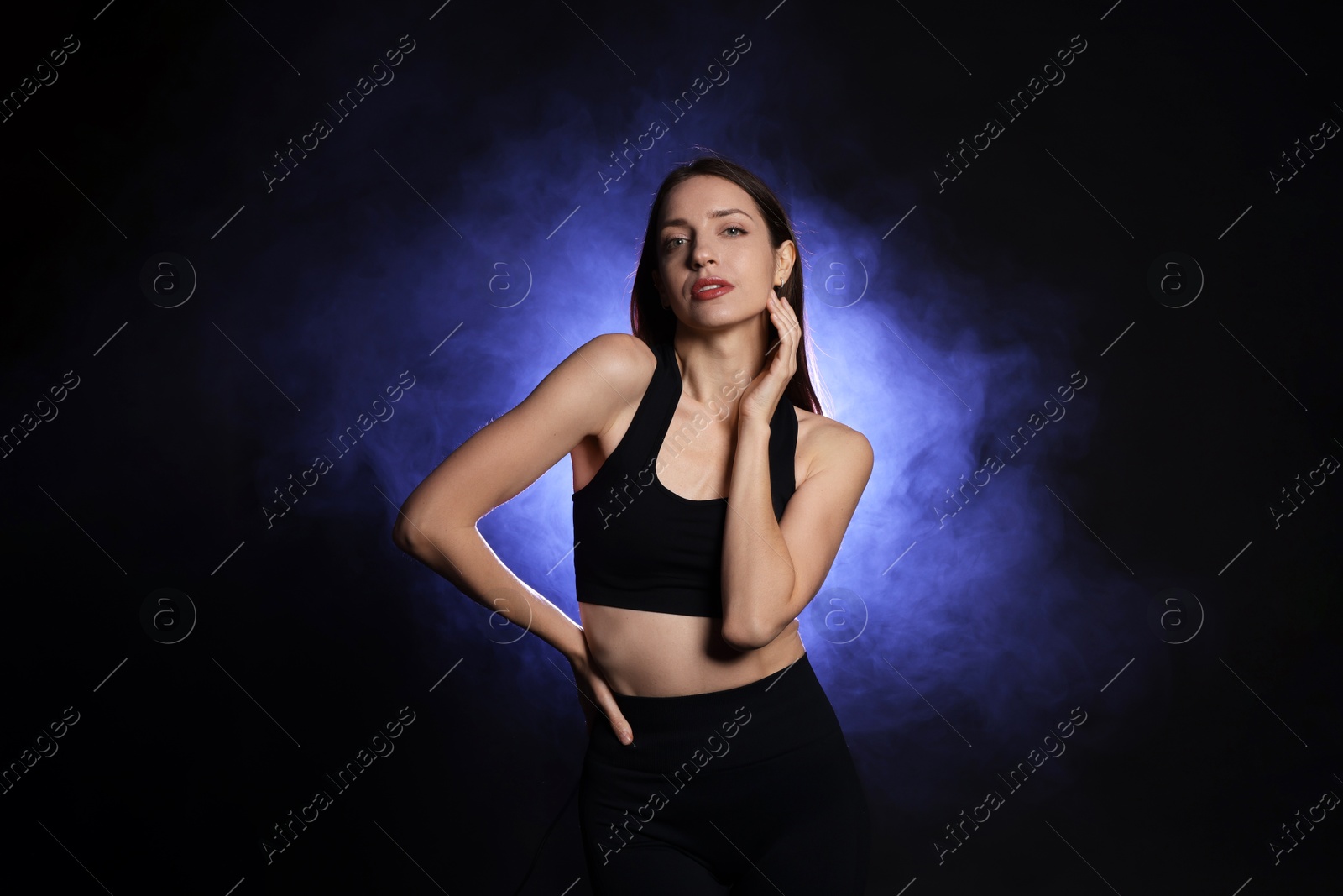 Photo of Beautiful woman in stylish sportswear on dark background with color light and smoke