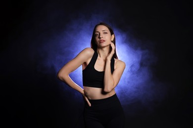 Photo of Beautiful woman in stylish sportswear on dark background with color light and smoke