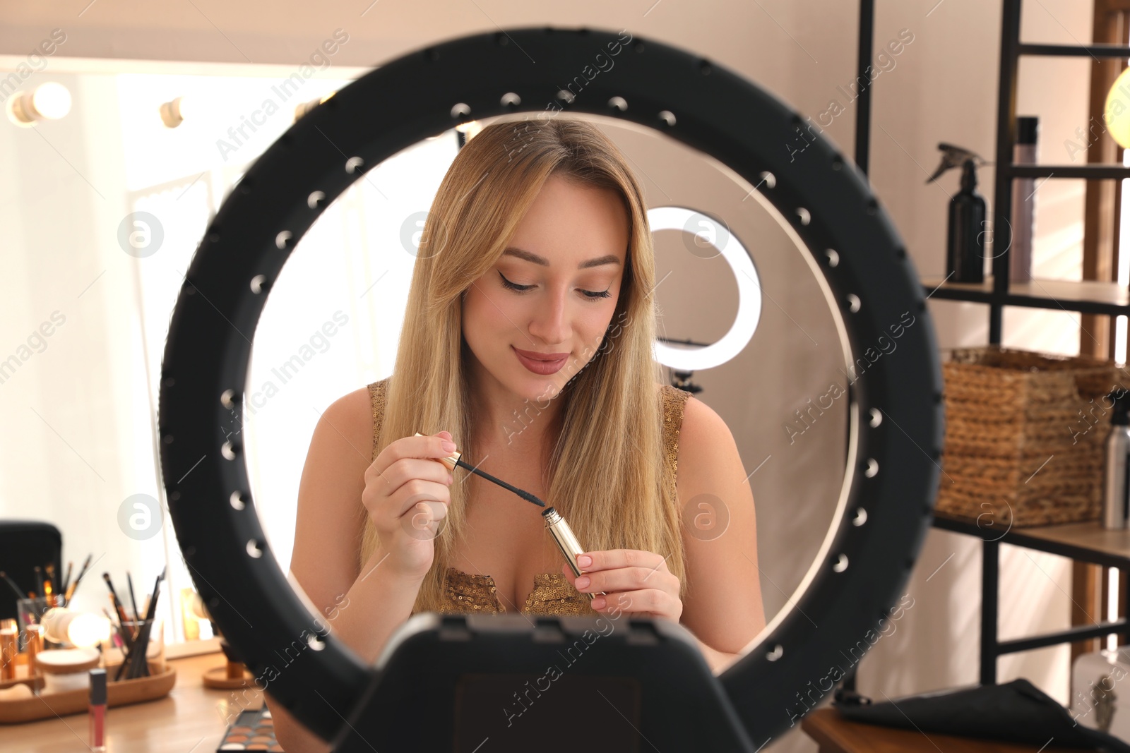 Photo of Beautiful young woman with mascara for eyelashes indoors, view through ring lamp