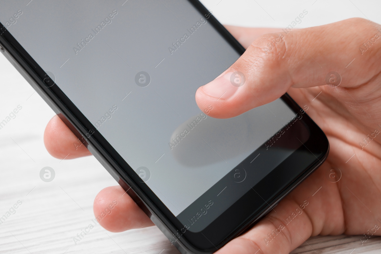 Photo of Man unlocking smartphone with fingerprint scanner at light wooden table, closeup