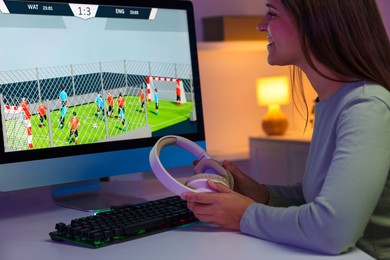 Photo of Smiling woman with headphones playing video game at table with keyboard indoors