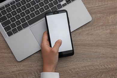 Photo of Woman unlocking smartphone with fingerprint scanner near laptop at wooden table, top view