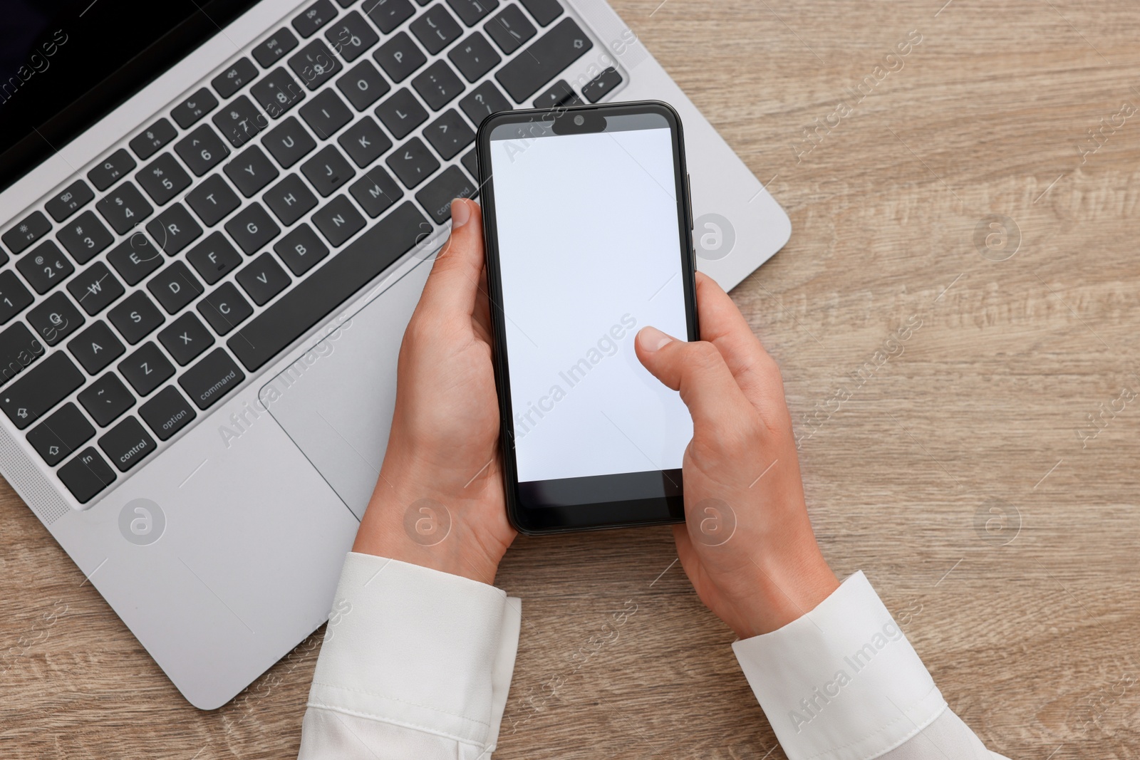 Photo of Woman unlocking smartphone with fingerprint scanner near laptop at wooden table, top view