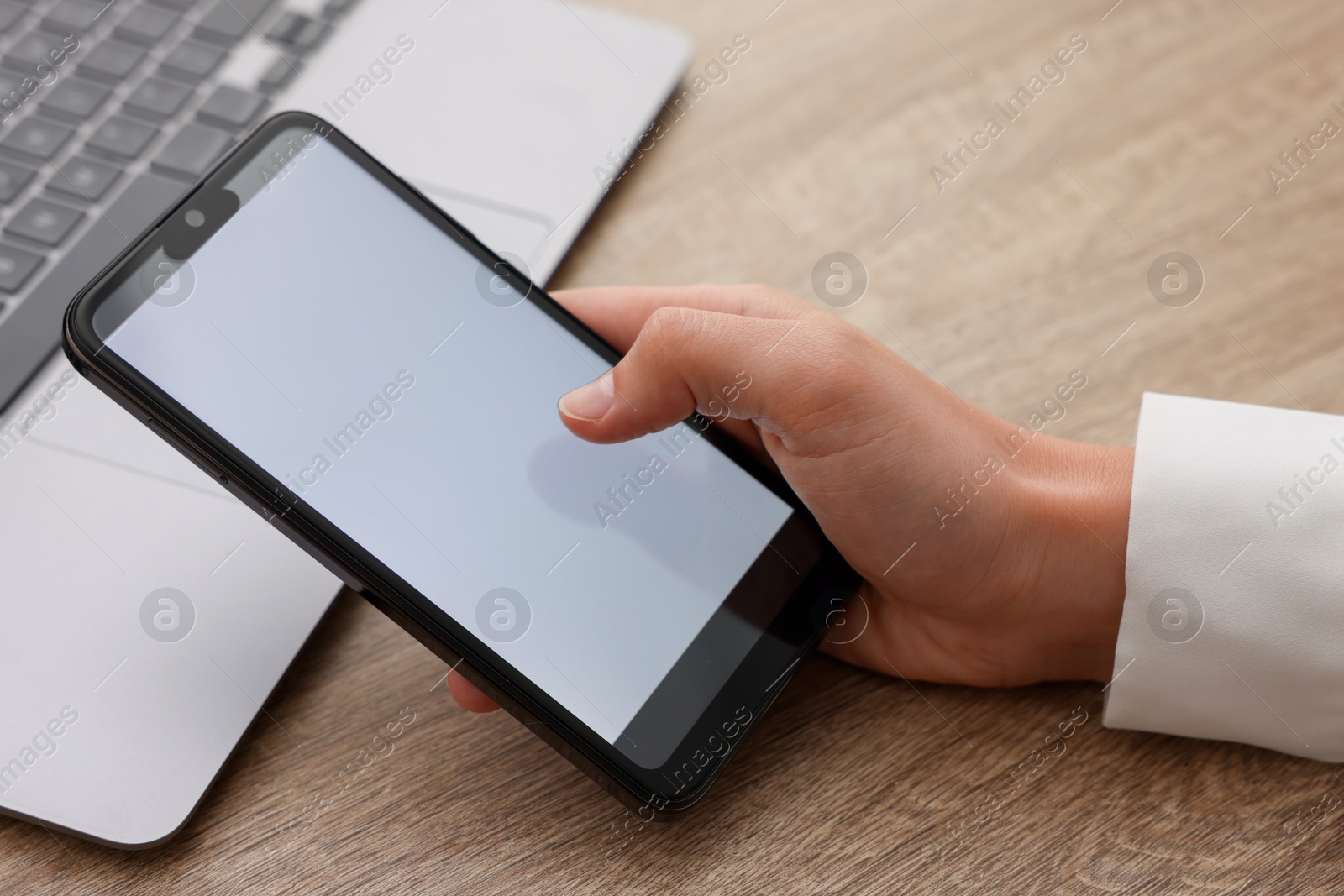 Photo of Woman unlocking smartphone with fingerprint scanner near laptop at wooden table, closeup