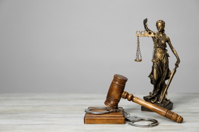 Photo of Handcuffs, judge's gavel and Lady Justice figure on white wooden table, space for text