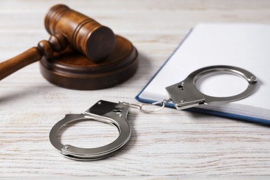 Photo of Handcuffs, judge's gavel and book on white wooden table, closeup