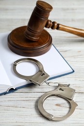 Photo of Handcuffs, judge's gavel and book on white wooden table, closeup