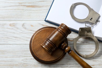 Photo of Handcuffs, judge's gavel and book on white wooden table