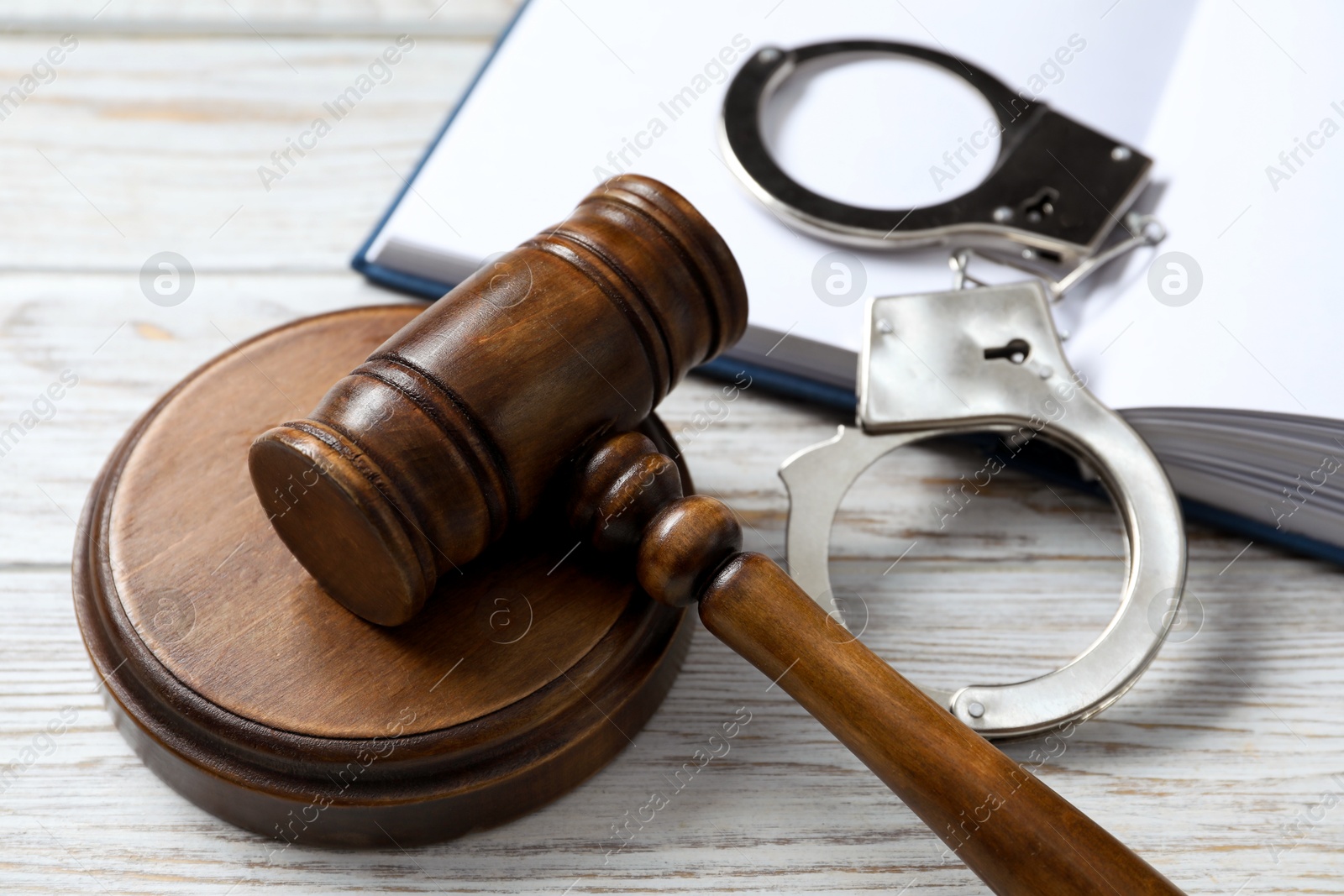 Photo of Handcuffs, judge's gavel and book on white wooden table, closeup