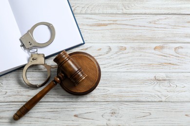 Photo of Handcuffs, judge's gavel and book on white wooden table, flat lay. Space for text