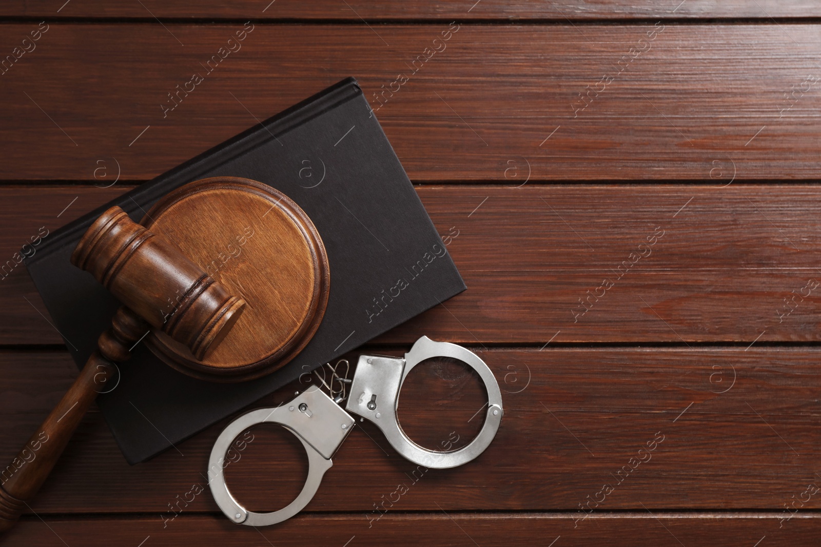 Photo of Handcuffs, judge's gavel and book on wooden table, flat lay. Space for text