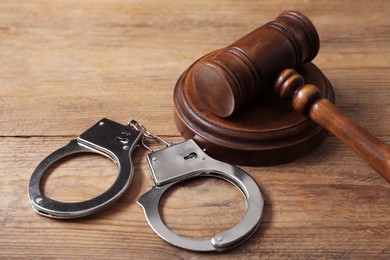 Photo of Handcuffs and judge's gavel on wooden table, closeup