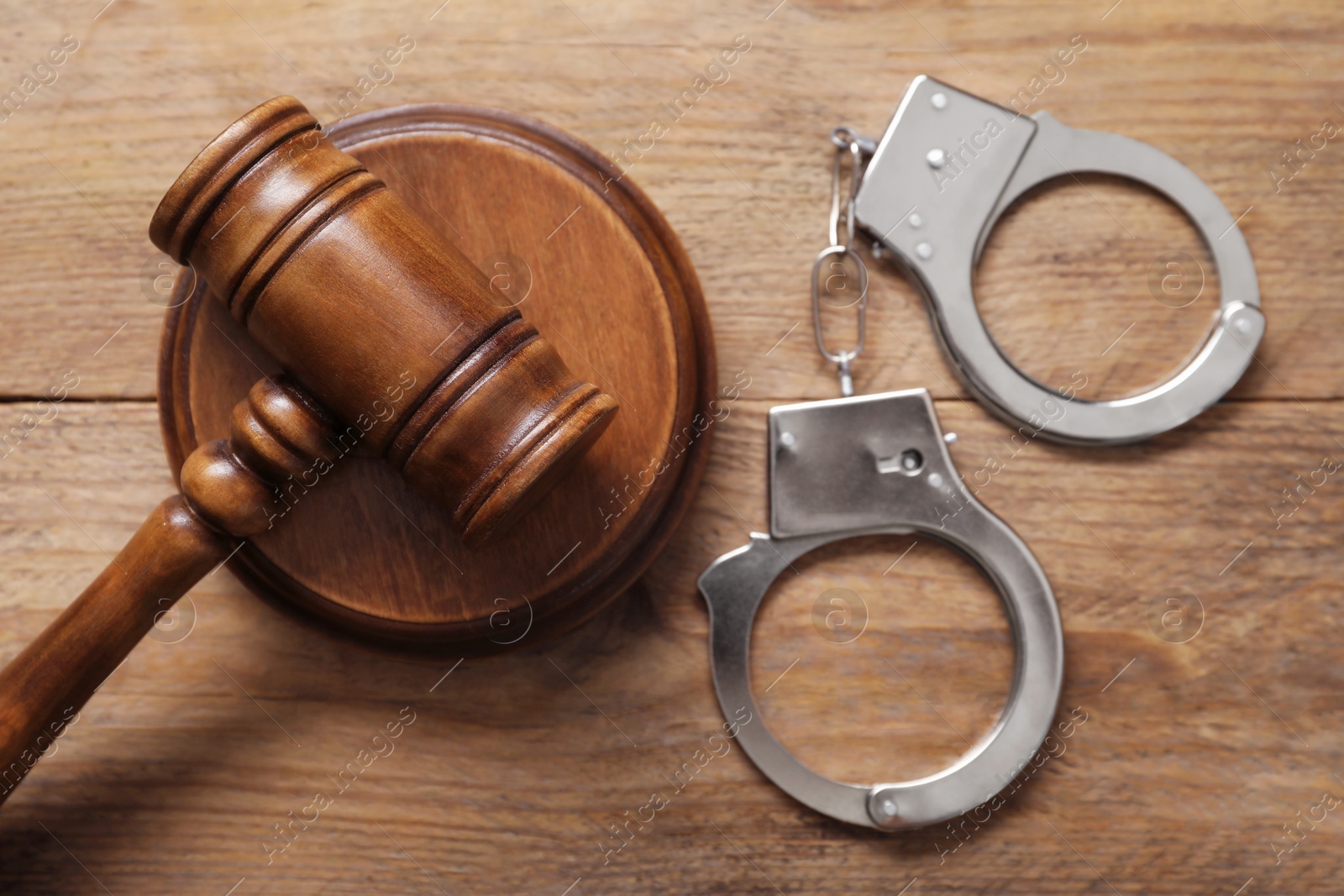 Photo of Handcuffs and judge's gavel on wooden table, flat lay