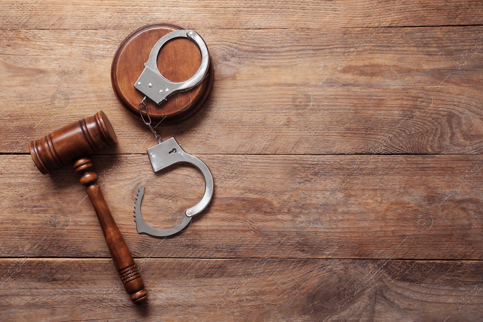 Photo of Handcuffs and judge's gavel on wooden table, flat lay. Space for text