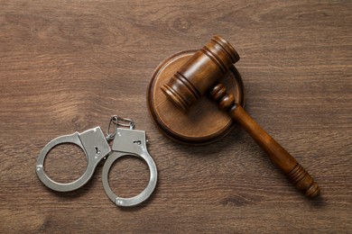 Photo of Handcuffs and judge's gavel on wooden table, flat lay