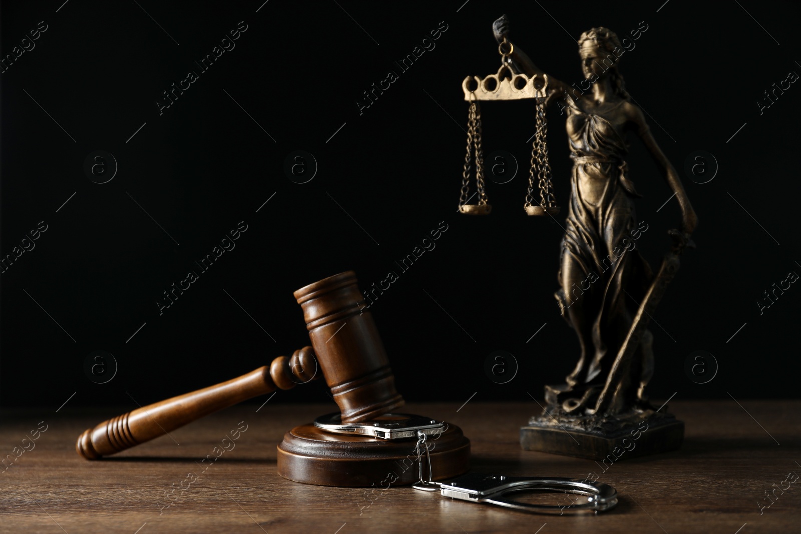 Photo of Handcuffs, judge's gavel and Lady Justice figure on wooden table