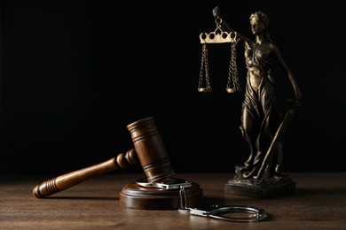 Photo of Handcuffs, judge's gavel and Lady Justice figure on wooden table