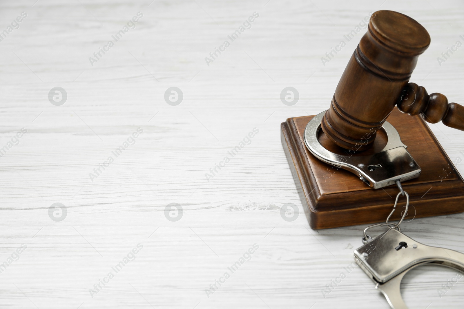 Photo of Handcuffs and judge's gavel on white wooden table, closeup. Space for text