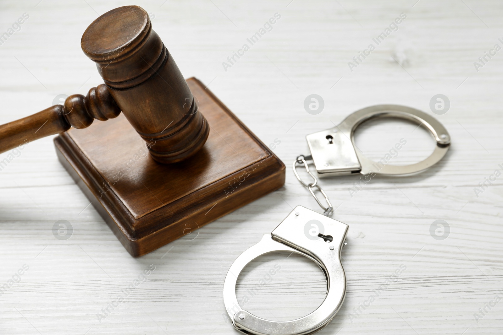 Photo of Handcuffs and judge's gavel on white wooden table, closeup