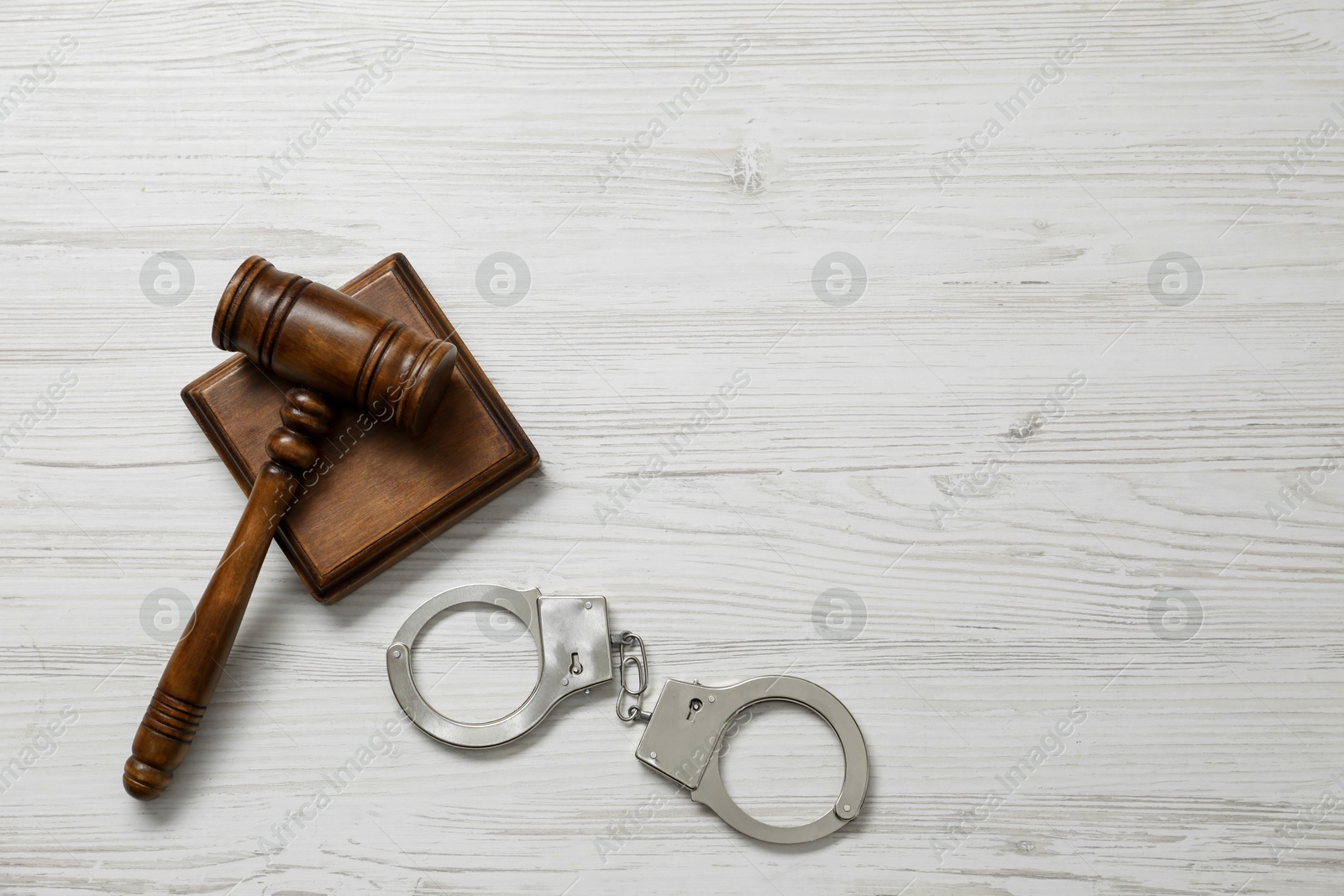 Photo of Handcuffs and judge's gavel on white wooden table, flat lay. Space for text