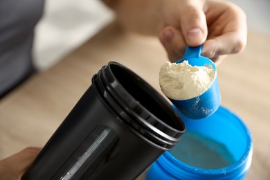 Photo of Making protein cocktail. Man adding powder into shaker at table, closeup