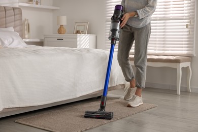 Photo of Young woman cleaning floor with cordless vacuum cleaner in bedroom, closeup