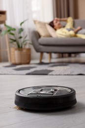 Photo of Young woman resting at home, focus on robotic vacuum cleaner