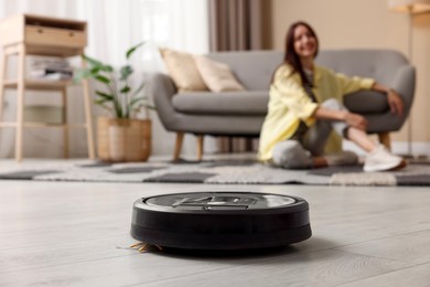 Young woman resting at home, focus on robotic vacuum cleaner