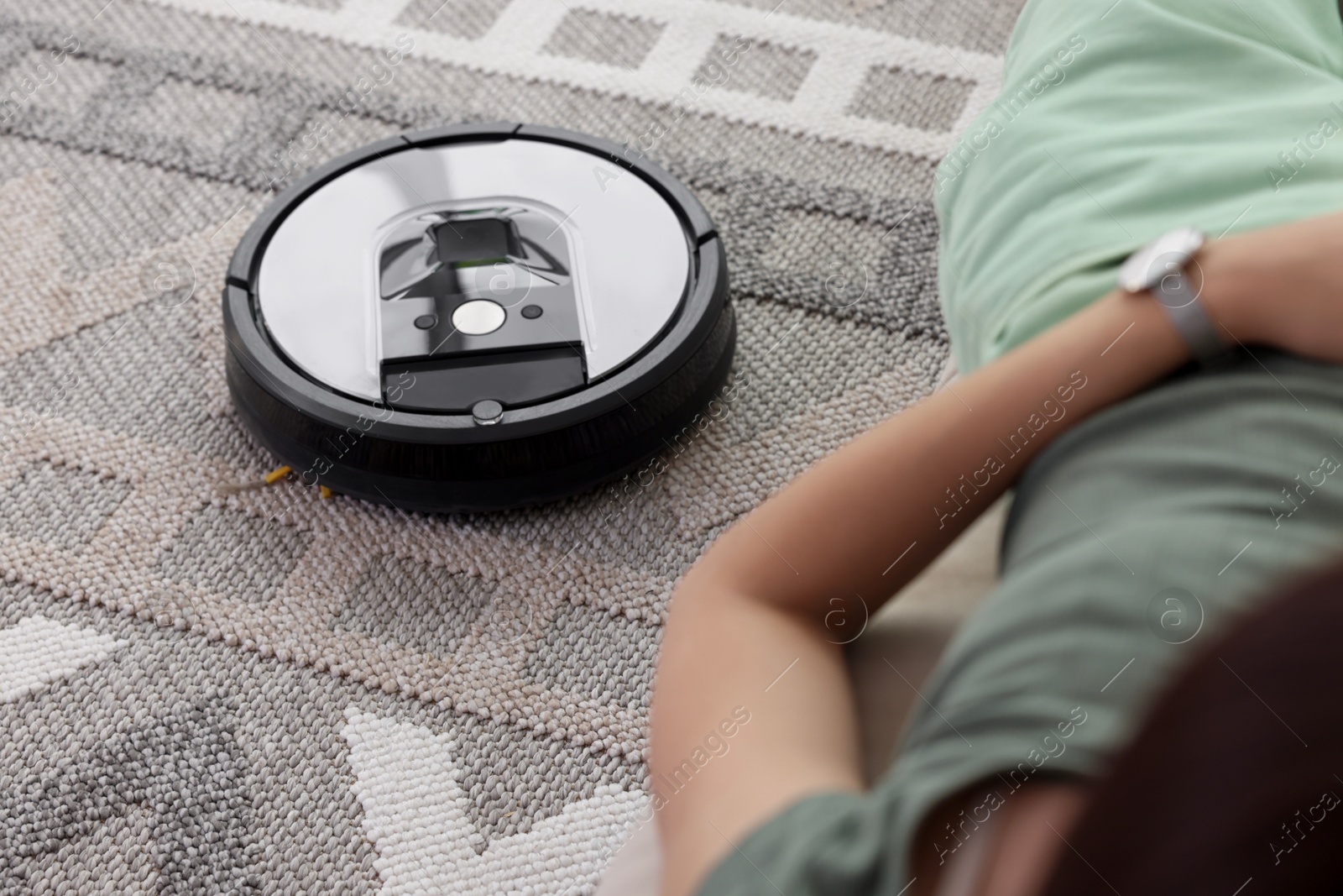 Photo of Young woman resting while robotic vacuum cleaner vacuuming rug at home, closeup