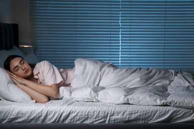 Photo of Young woman sleeping in soft bed at night