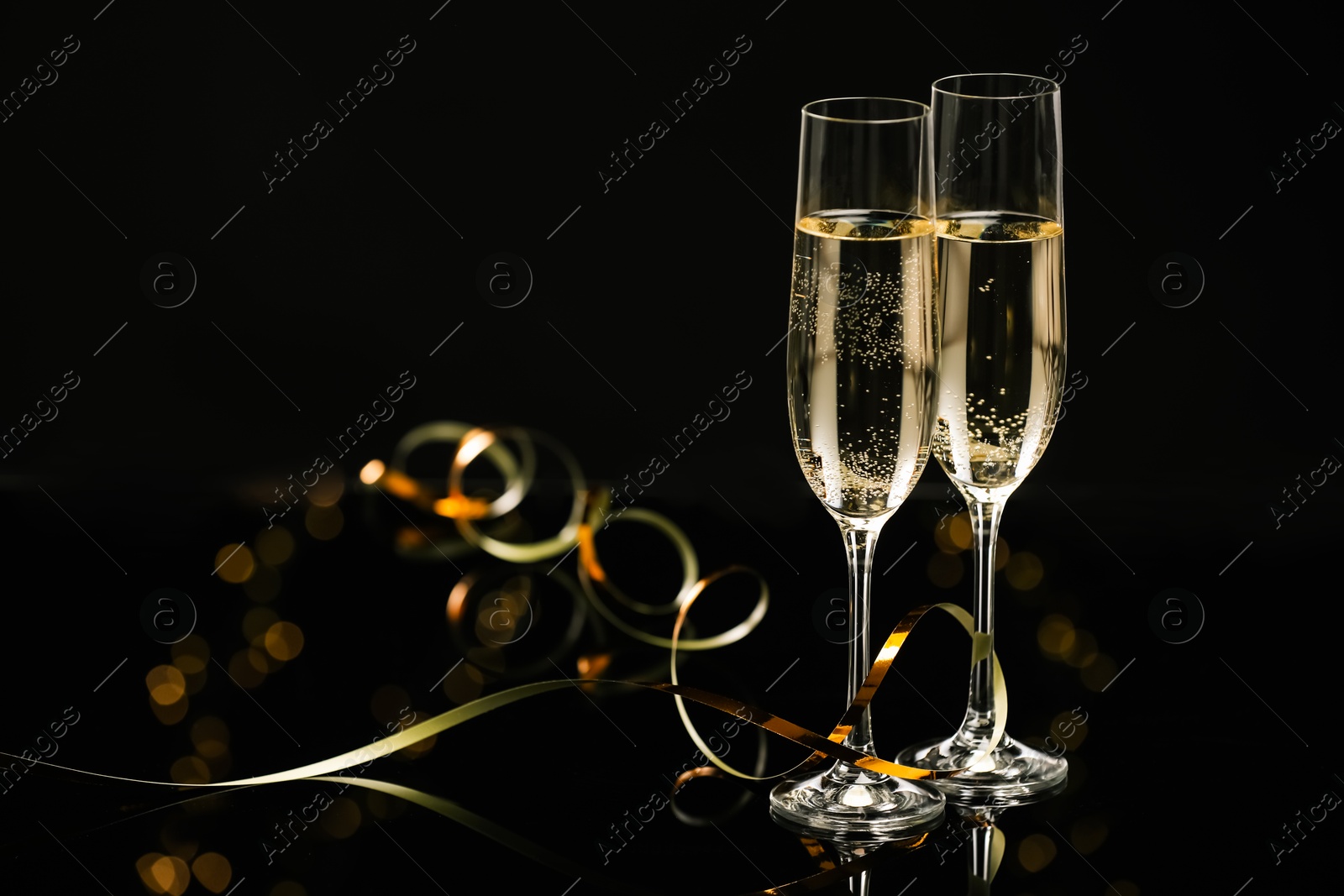 Photo of Champagne in glasses and party streamers on black mirror surface, space for text