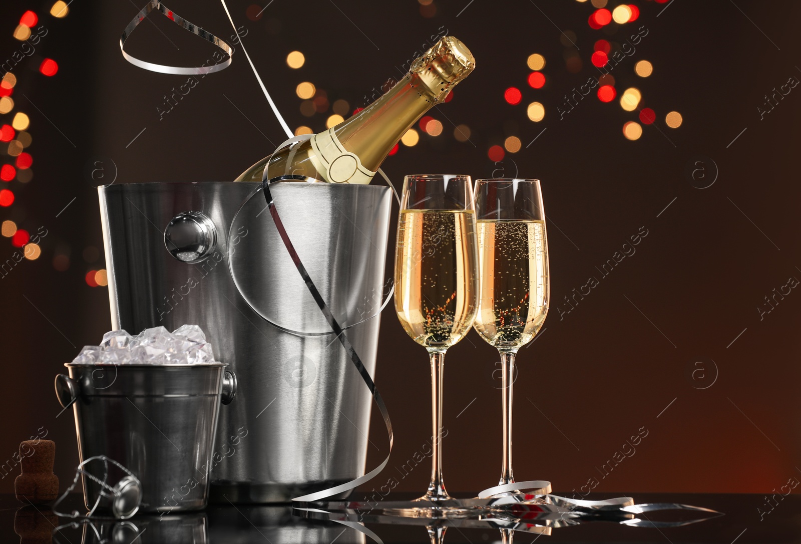 Photo of Champagne in glasses, bottle and ice buckets on mirror surface against color background with blurred lights, space for text