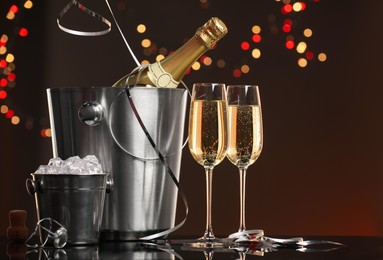 Photo of Champagne in glasses, bottle and ice buckets on mirror surface against color background with blurred lights, space for text