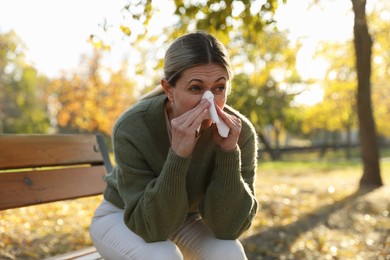 Photo of Woman with runny nose on wooden bench in park