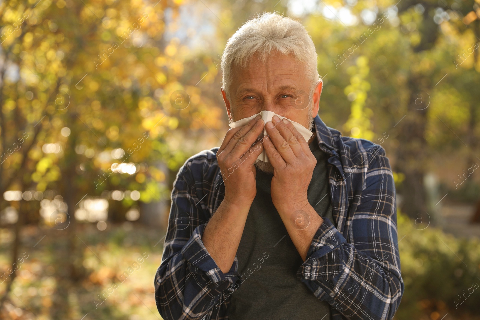 Photo of Senior man with tissue blowing runny nose in park