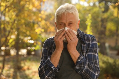 Photo of Senior man with tissue blowing runny nose in park