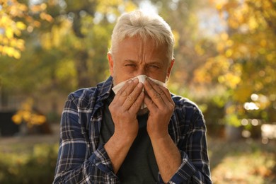 Photo of Senior man with tissue blowing runny nose in park