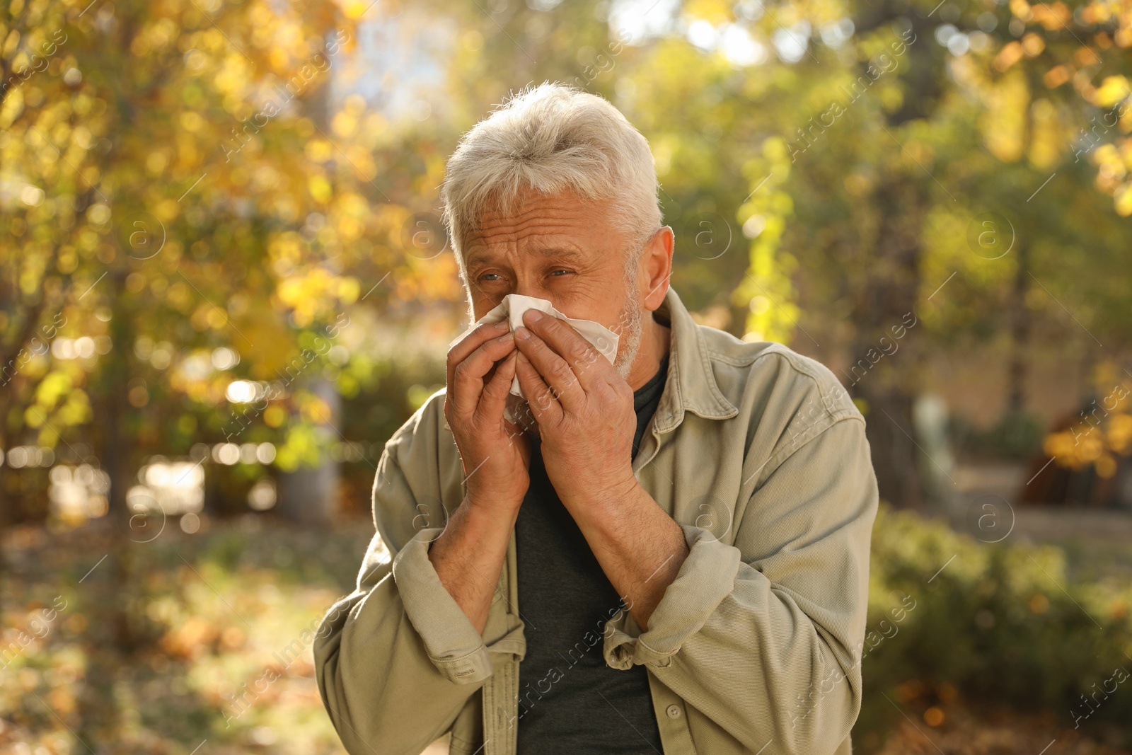 Photo of Senior man with tissue blowing runny nose in park